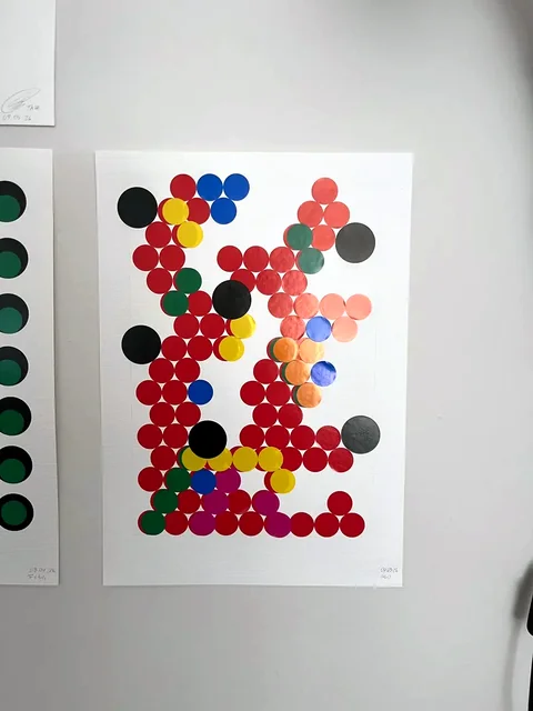 Nr. 12 – An der Wand: eine lockere Figur aus roten, schwarzen und farbigen Punkten auf weißem Papier